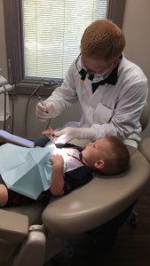 Dr. Stephen Wilson wearing safety loupes performing a dental checkup on a young child lying in a clinic treatment chair.