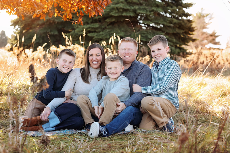 Dr. Stephen Wilson sitting outdoors in a grassy field with his wife and three sons for a family portrait.